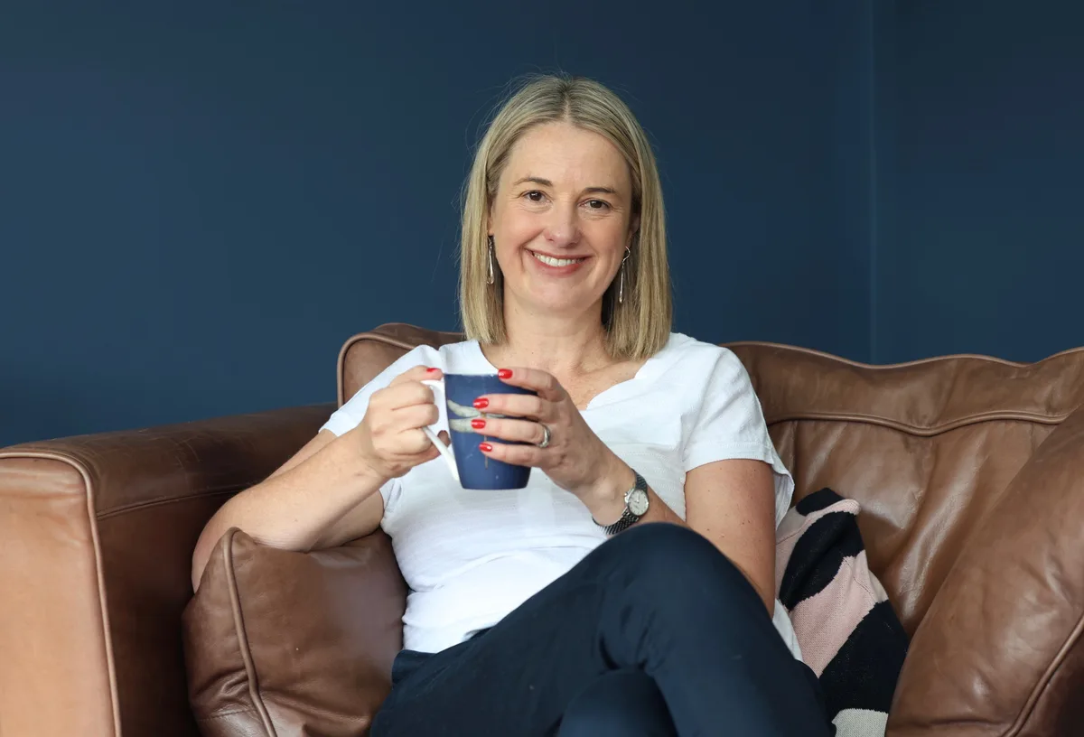 Laura smiling with a mug while relaxing on a sofa
