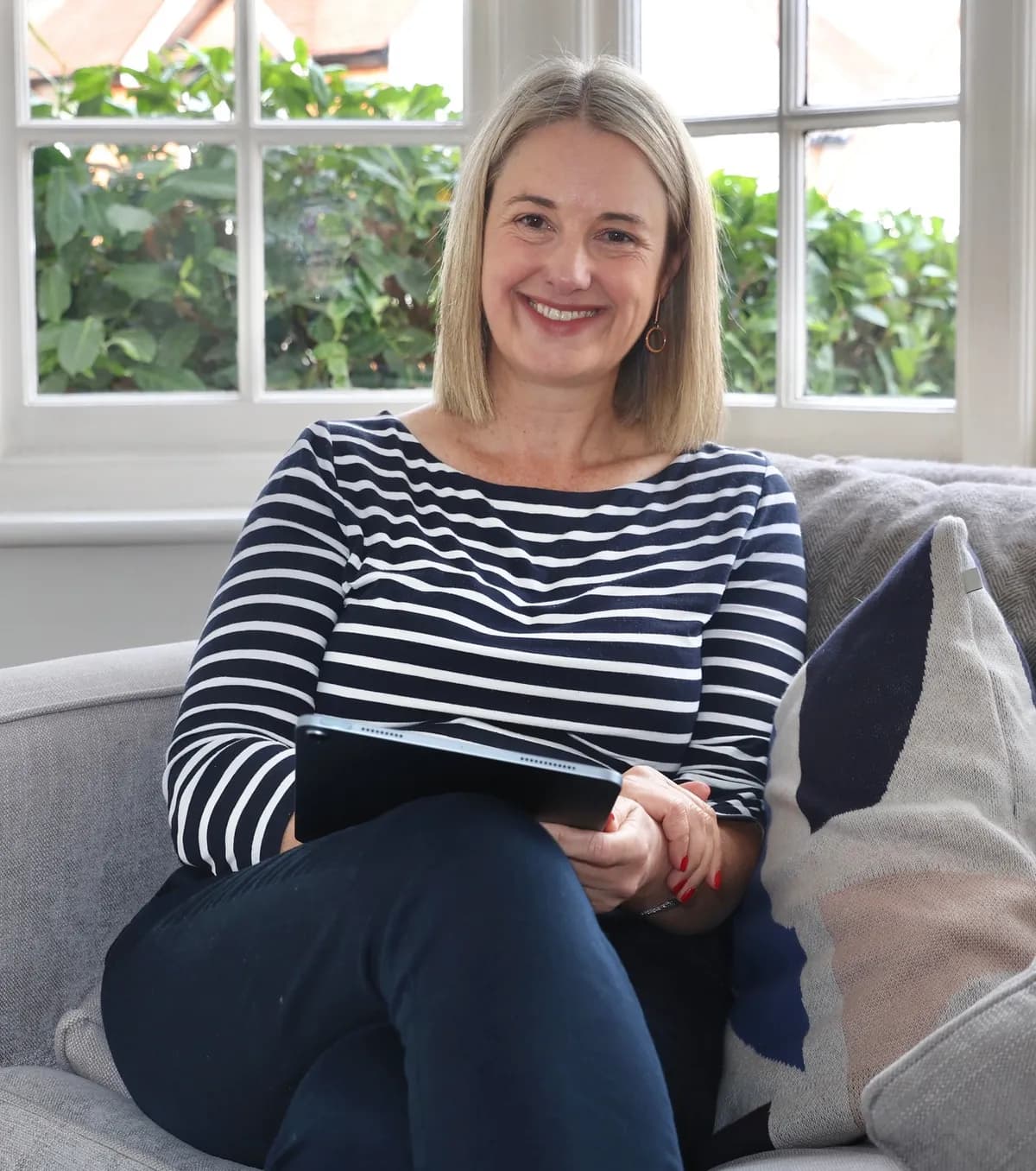 Laura smiling on a sofa with a tablet, ready for an online coaching session